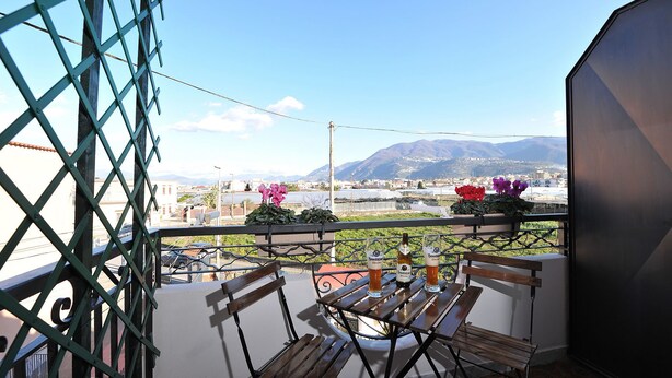 Un balcón con un banco de madera y dos botellas de cerveza, con vistas a un paisaje urbano y montañas al fondo.