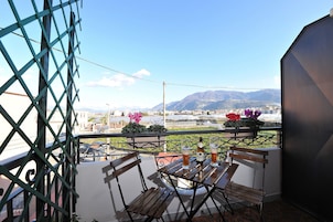 Un balcón con un banco de madera y dos botellas de cerveza, con vistas a un paisaje urbano y montañas al fondo.