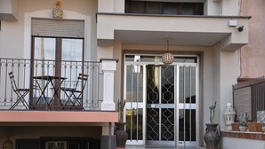 Un edificio de dos plantas con un balcón, una puerta principal grande con paneles de vidrio decorativos y una pequeña escalera que conduce a la entrada.
