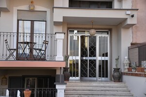 Un edificio de dos plantas con un balcón, una puerta principal grande con paneles de vidrio decorativos y una pequeña escalera que conduce a la entrada.