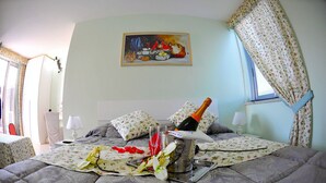 Un dormitorio con una cama, un cuadro, una botella de champán y una cortina estampada con motivos florales.