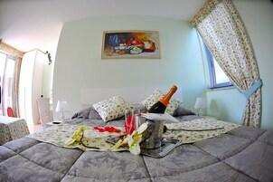 Un dormitorio con una cama, un cuadro, una botella de champán y una cortina estampada con motivos florales.