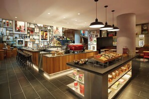 A modern bar area with stools, a counter with food and drinks, and shelves with various items. - citizenM New York Bowery (New York)