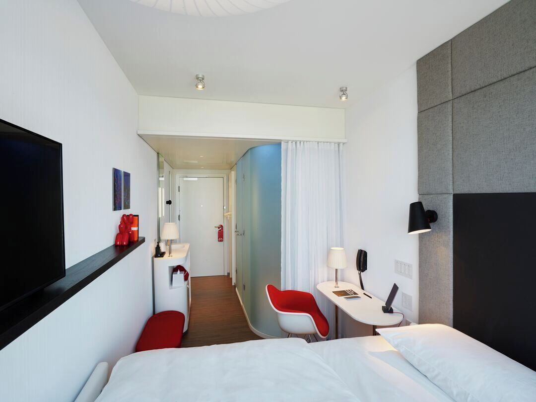 Une chambre d’hôtel avec un lit, un bureau et une chaise, une télévision, et une salle de bain visible au fond.