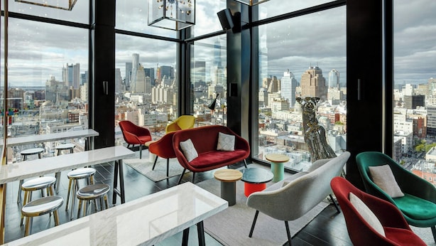 A modern interior with large windows offering a cityscape view, contemporary furniture, and a mix of red and neutral tones. - citizenM New York Bowery (New York)