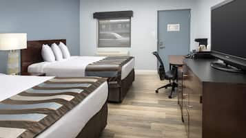 A hotel room with two beds, a desk, a chair, a television, and a window with a view of a street.