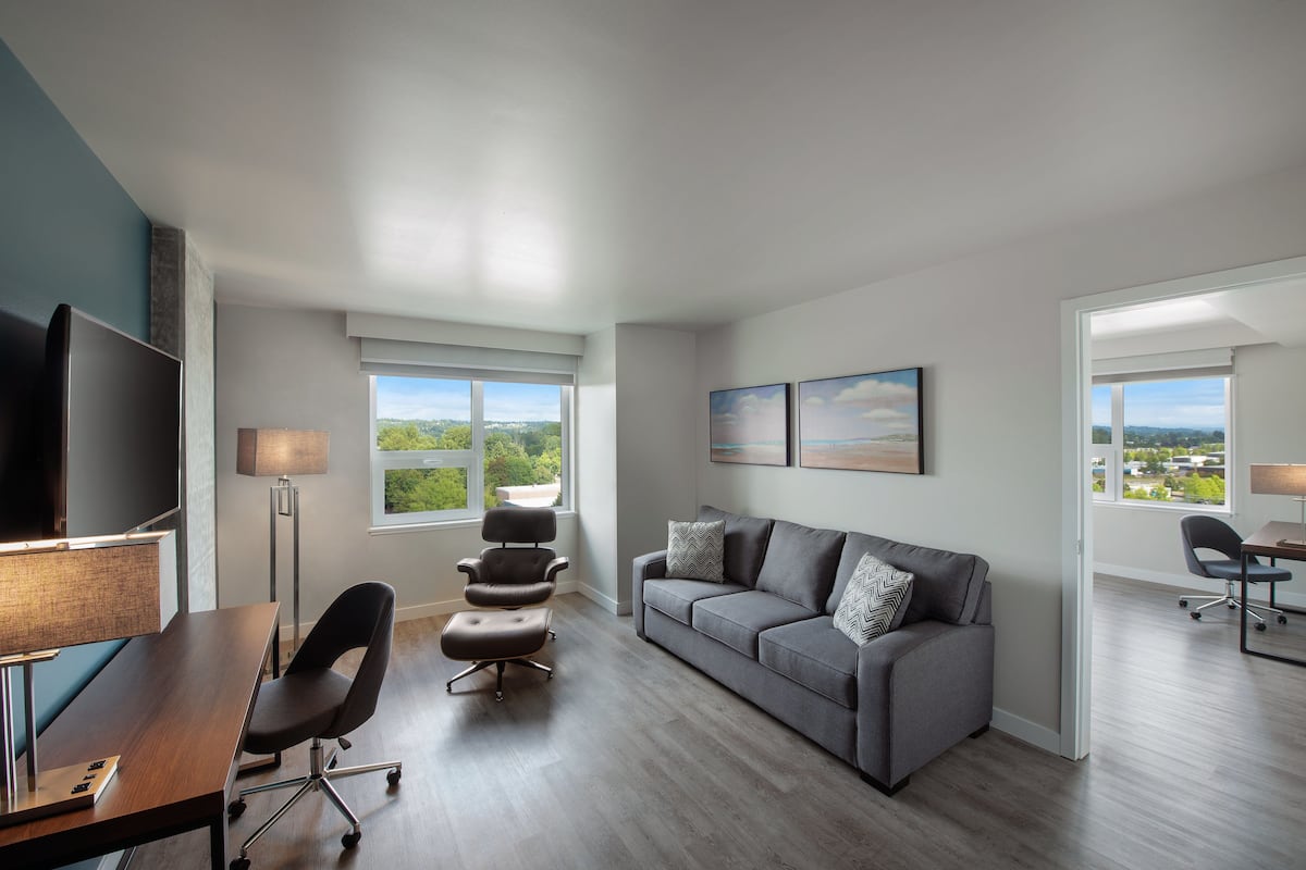 A modern living room with a grey sofa, a flat-screen TV, a desk, and a chair.