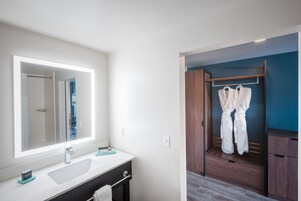 Un baño moderno con un espejo grande, un lavamanos y un vestidor con albornoces colgados.