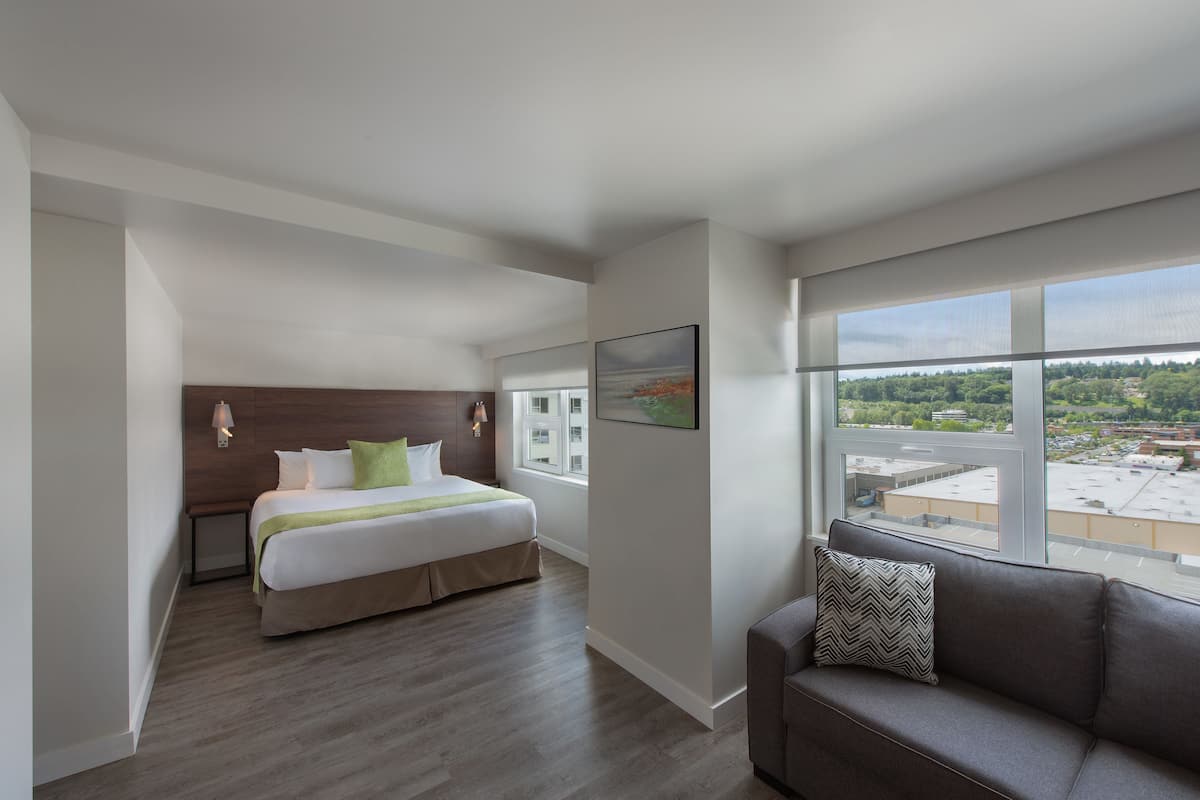 A modern hotel room with a large bed, a sofa, and a view of the city.