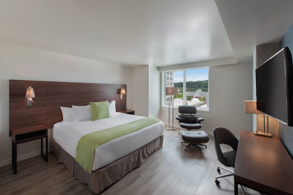 A hotel room with a large bed, a desk, a chair, and a TV.