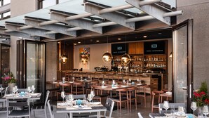 An outdoor dining area with tables and chairs, a bar with bottles, and a modern interior design. - Hotel Interurban Seattle Airport SeaTac (Tukwila)