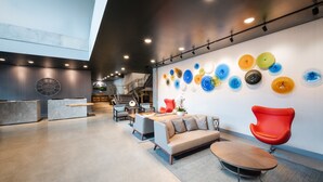 A modern lobby with a sofa, chairs, a coffee table, and a wall with colorful glass art. - Hotel Interurban Seattle Airport SeaTac (Tukwila)