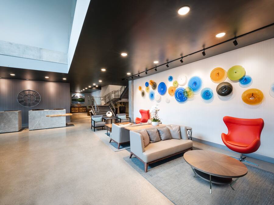 A modern lobby with a sofa, chairs, a coffee table, and a wall with colorful glass art.