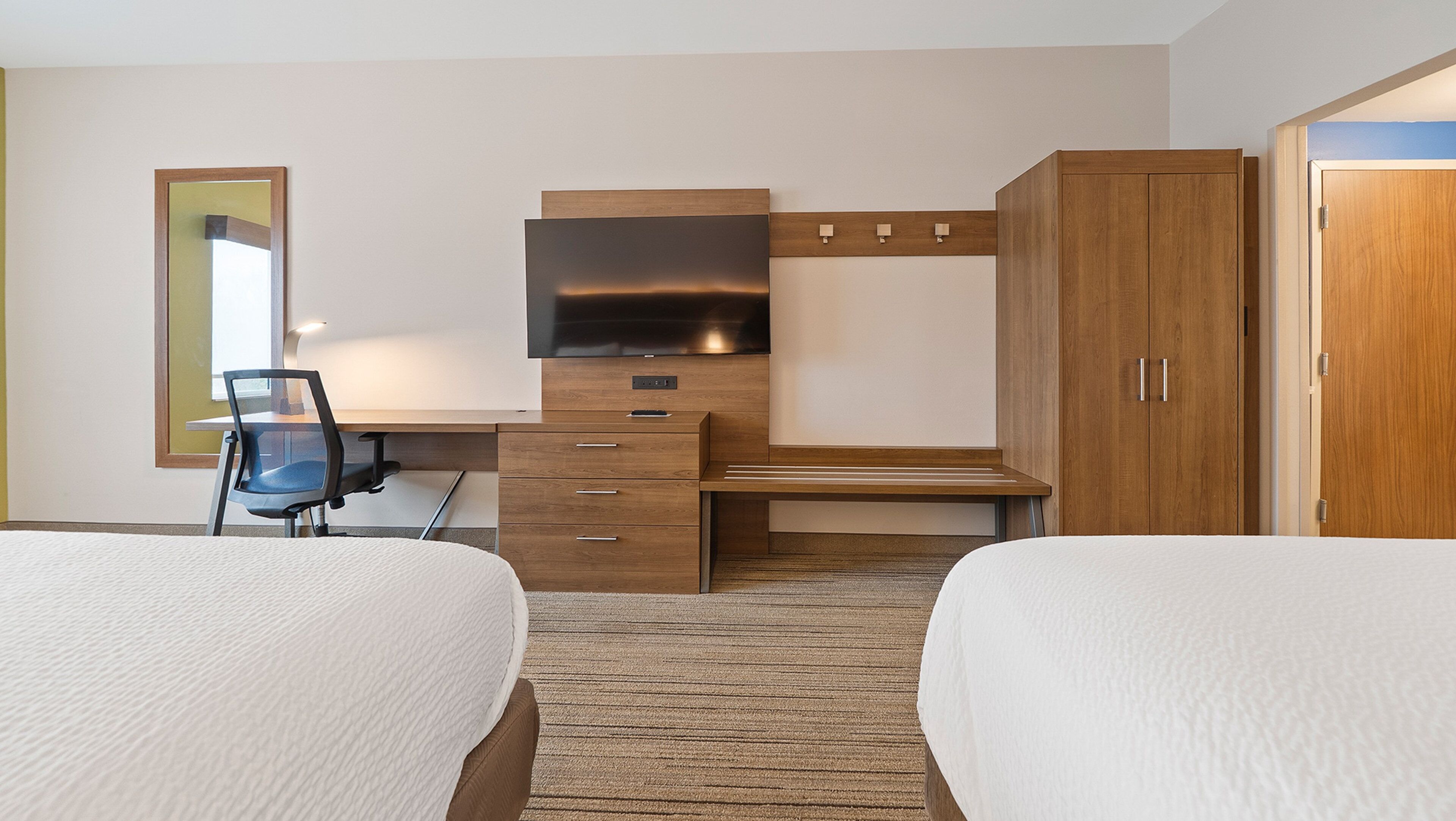 A hotel room with two beds, a desk with a chair, a television, and a wardrobe.