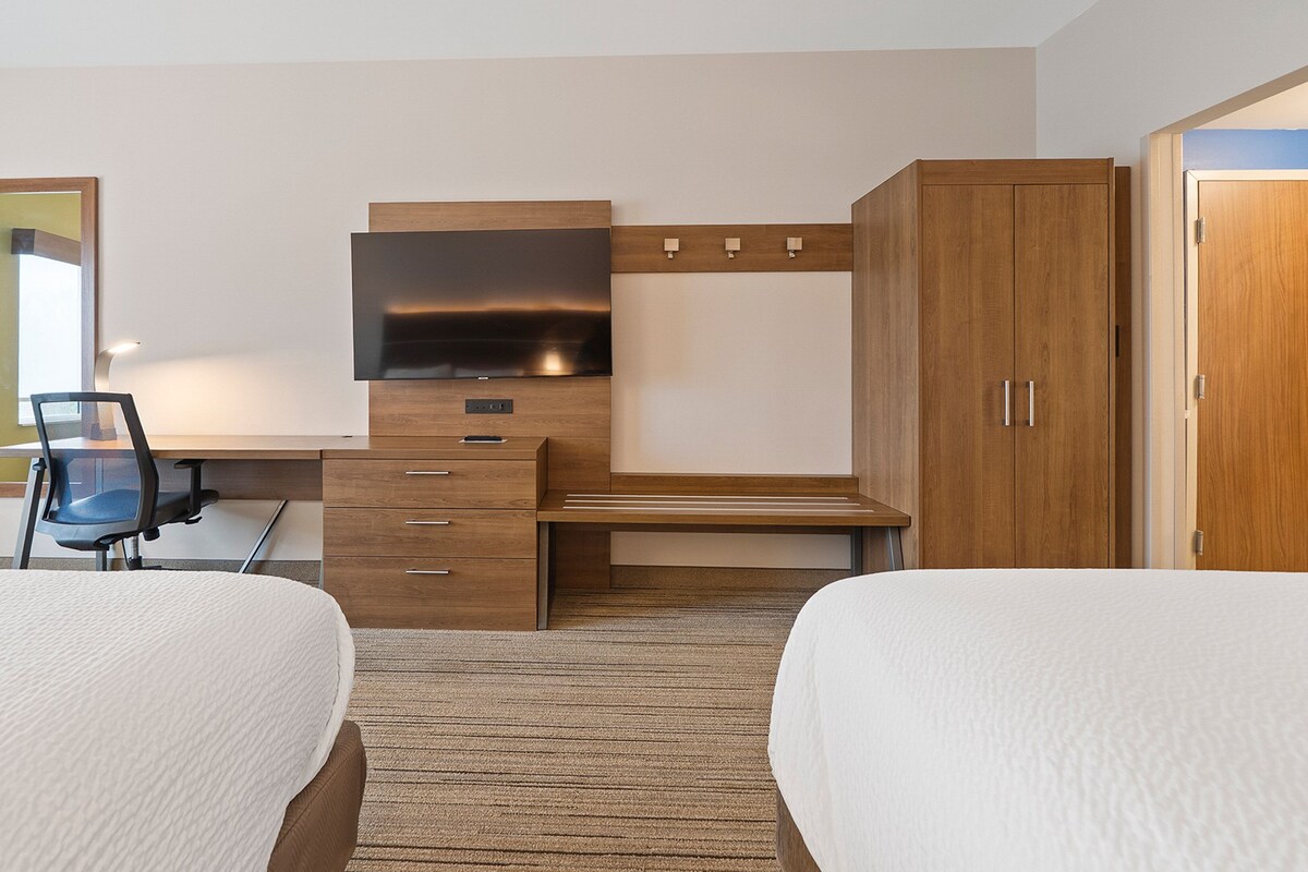 A hotel room with two beds, a desk with a chair, a television, and a wardrobe.