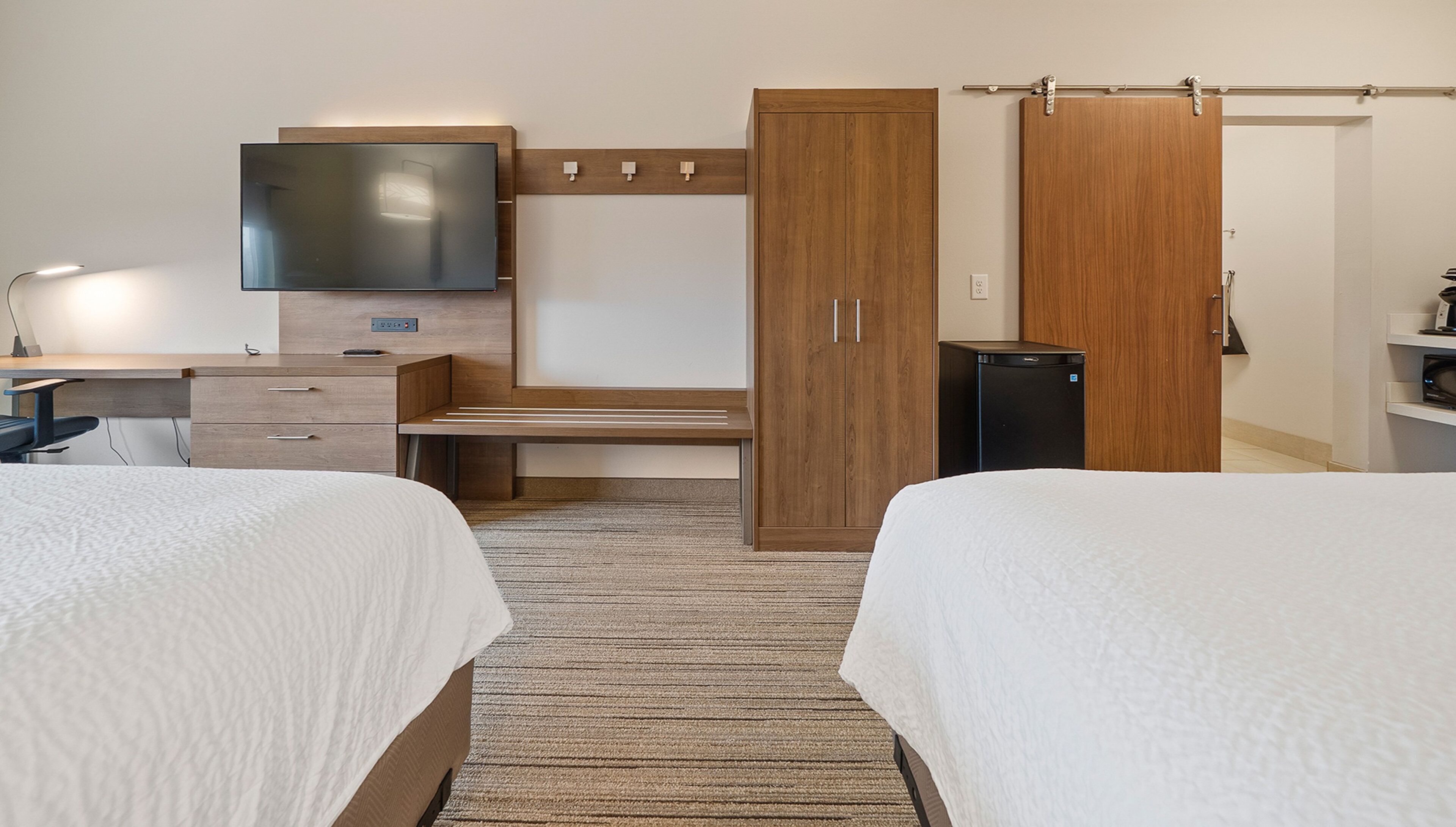 A hotel room with two beds, a desk, a television, a wardrobe, and a refrigerator.