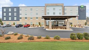 A Holiday Inn Express & Suites building with a covered entrance, multiple parking spaces, and landscaped areas with shrubs and rocks. - Holiday Inn Express & Suites Macon North by IHG (Macon)