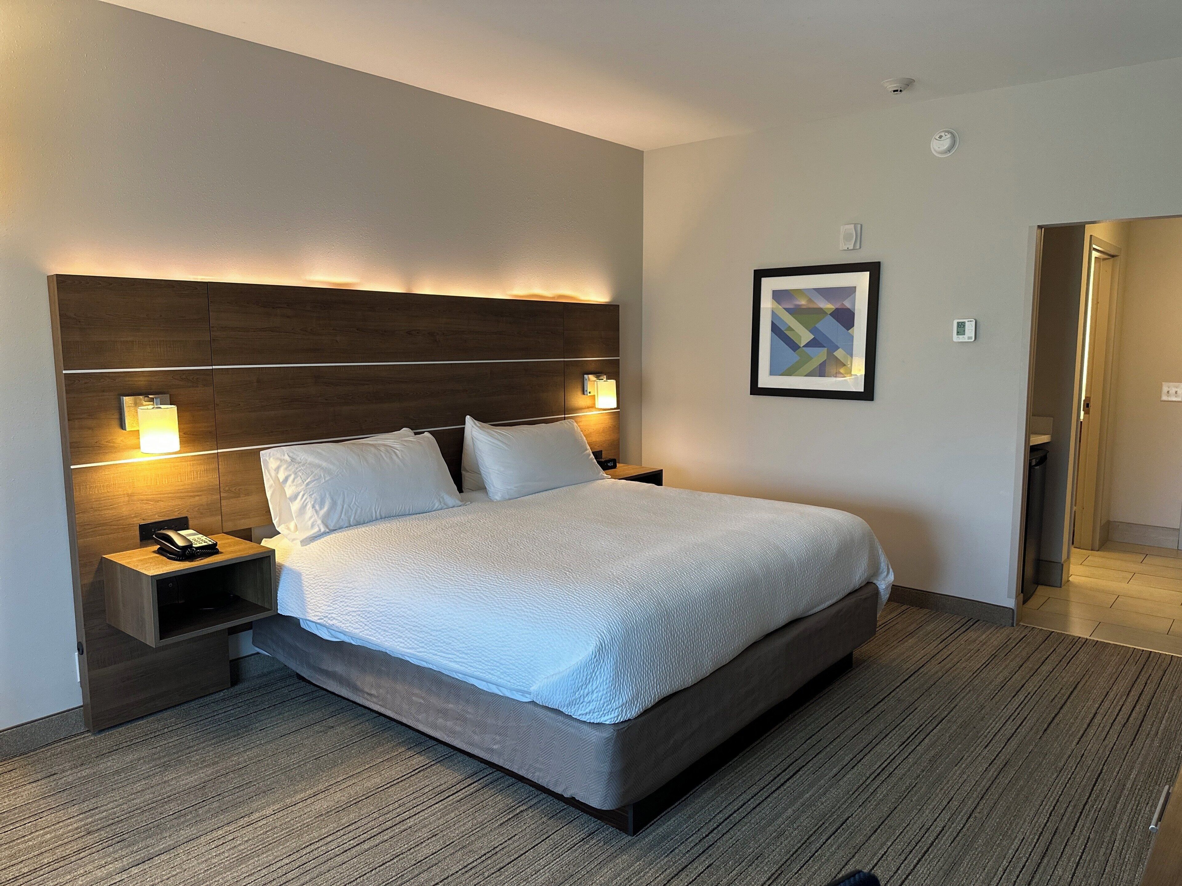 Ein Hotelzimmer mit einem großen Bett, zwei Nachttischen mit Lampen, einem Telefon und einem gerahmten abstrakten Gemälde an der Wand.