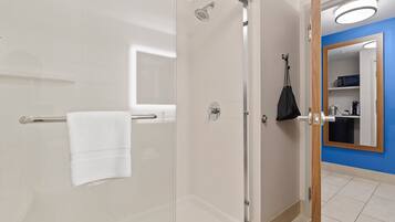 Un bagno moderno con cabina doccia in vetro, un asciugamano bianco su un porta asciugamani, una borsa nera appesa alla porta e una parete blu con uno specchio.