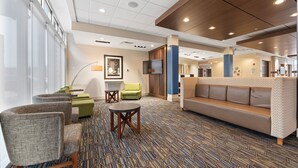 A hotel lobby with a patterned carpet, seating area with sofas and chairs, a reception desk, and a television on the wall. - Holiday Inn Express & Suites Macon North by IHG (Macon)