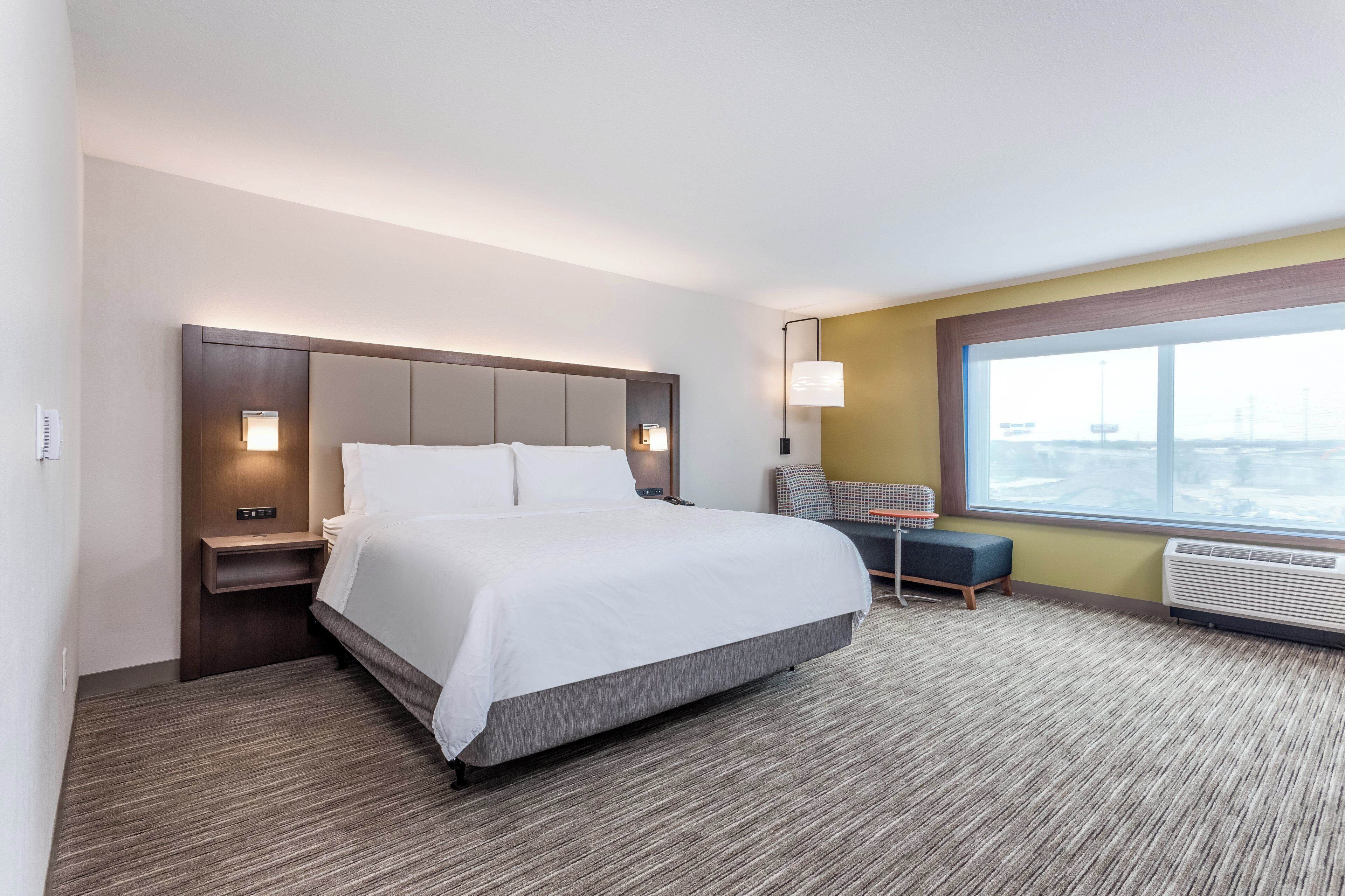 Habitación de hotel con una cama grande, una mesita de noche, un escritorio con silla, una ventana con vistas y un calentador en la pared.