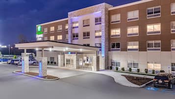 Een Holiday Inn Express & Suites hotel met een overdekte ingang, stenen zuilen en een parkeerplaats.