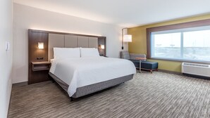 Une chambre d’hôtel avec un grand lit, une table de chevet, un bureau, une chaise et une fenêtre donnant sur la ville.