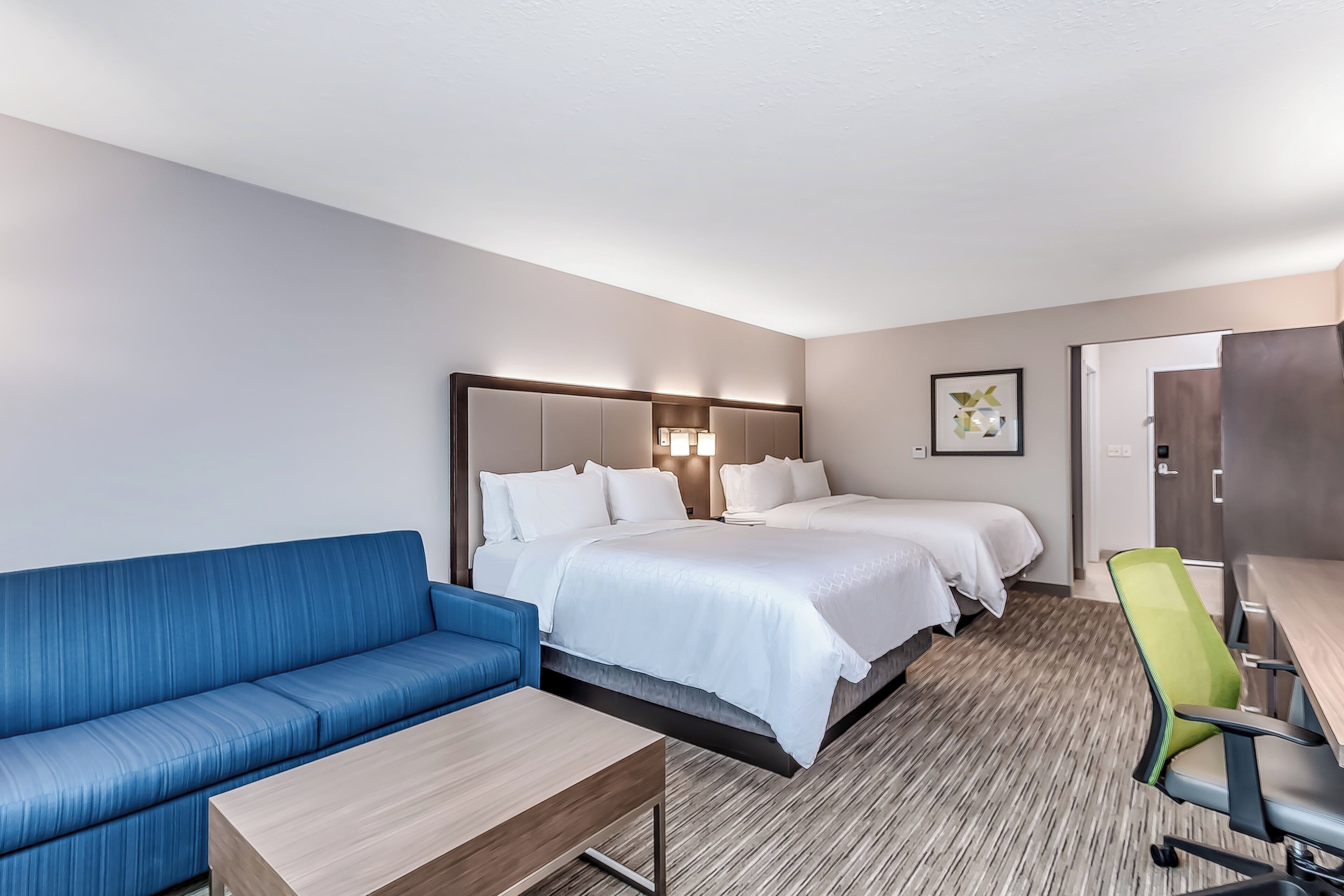 A hotel room with a bed, a blue sofa, a desk, and a chair.