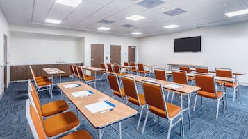 Un salón de conferencias con filas de mesas y sillas, un televisor de pantalla plana y una puerta con la inscripción 'STORAGE'.
