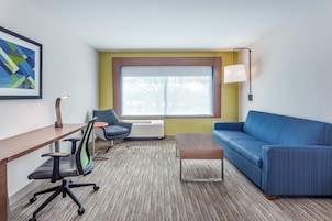 Una habitación de hotel moderna con un ventanal grande, un sofá azul, un escritorio de madera, una silla y una lámpara.