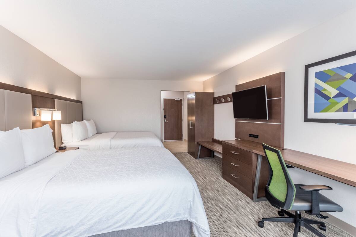 Une chambre d’hôtel avec deux lits, un bureau, une chaise, une télévision et une porte donnant sur une autre pièce.