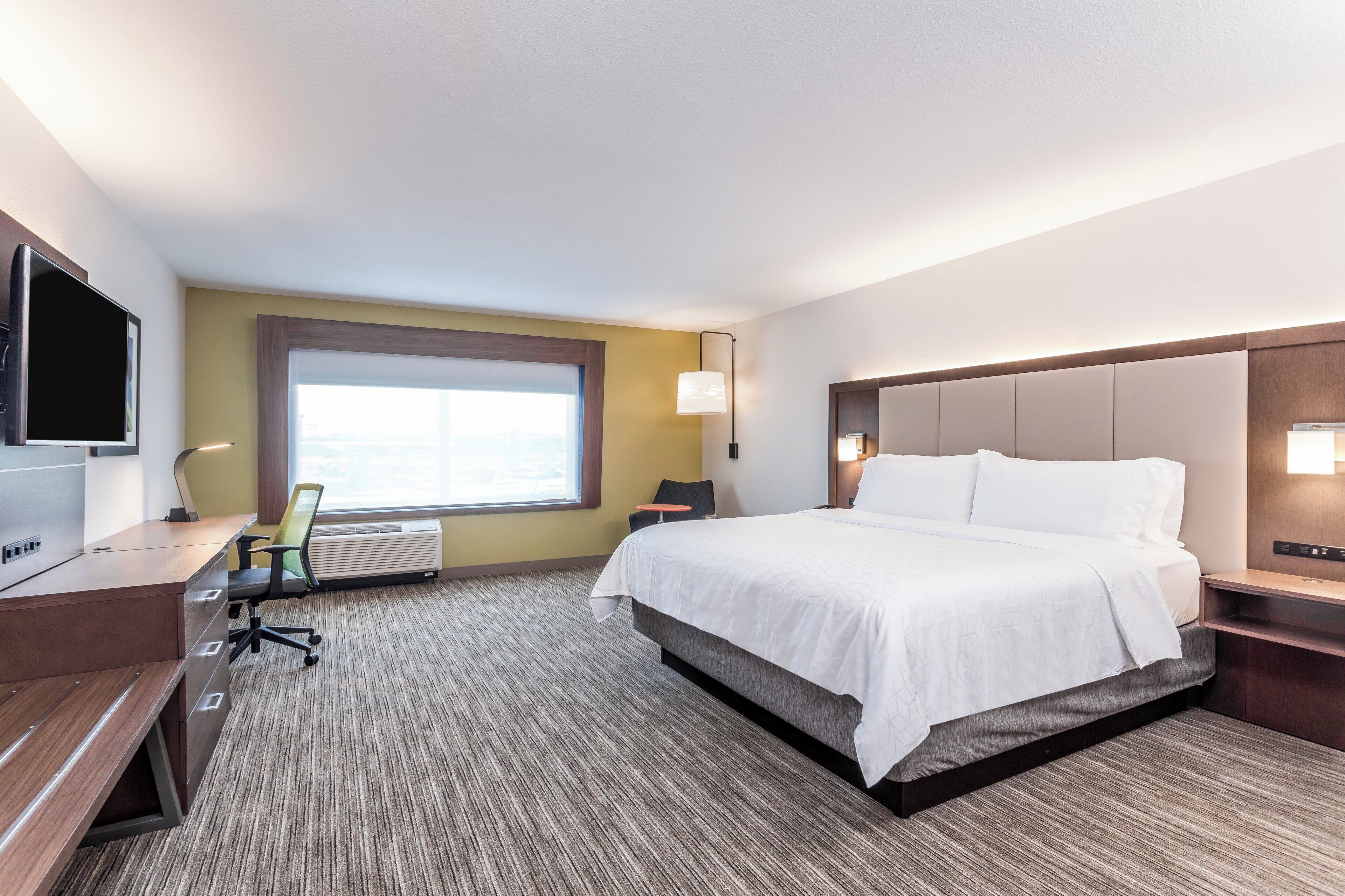 Una habitación de hotel con cama, escritorio, silla, televisor y ventana.
