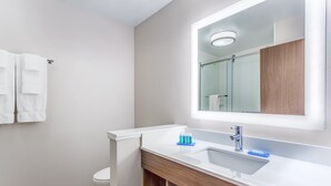 Une salle de bain moderne avec un lavabo blanc, un miroir et une cabine de douche en verre.