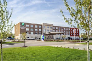 A Holiday Inn Express & Suites hotel with a modern design, featuring a parking lot, a landscaped entrance area, and a clear sky.