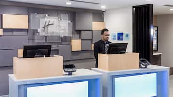 Un comptoir d’accueil d’hôtel équipé d’un terminal d’enregistrement numérique, d’un écran d’ordinateur et d’un panneau fixé au mur.