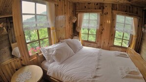 Un dormitorio de cabaña de madera con una cama, dos ventanas y una mesita.