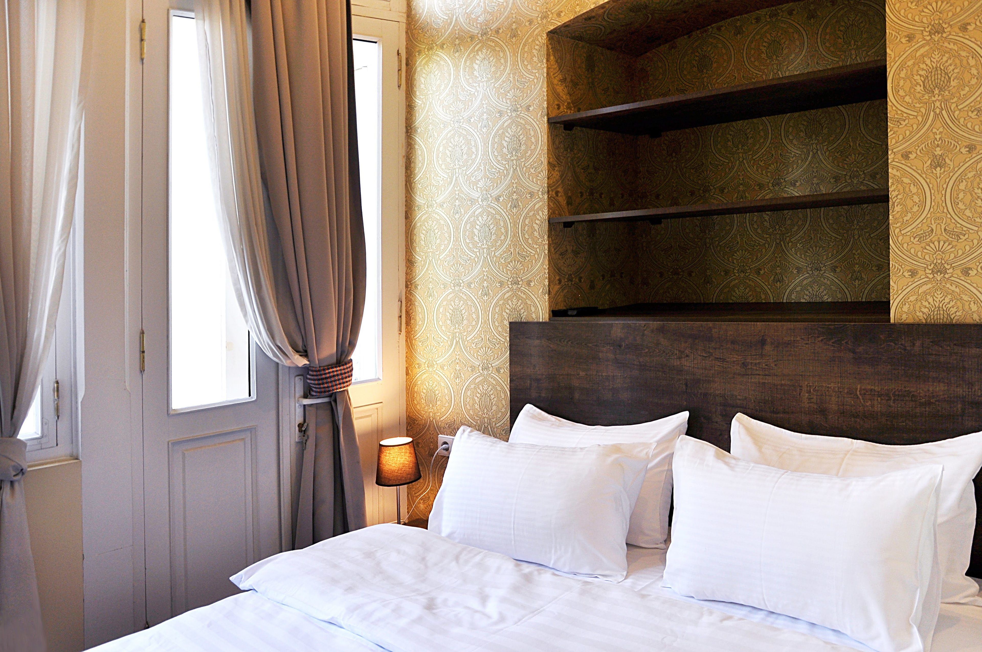 A hotel room with a bed, a nightstand with a lamp, and a headboard with shelves.