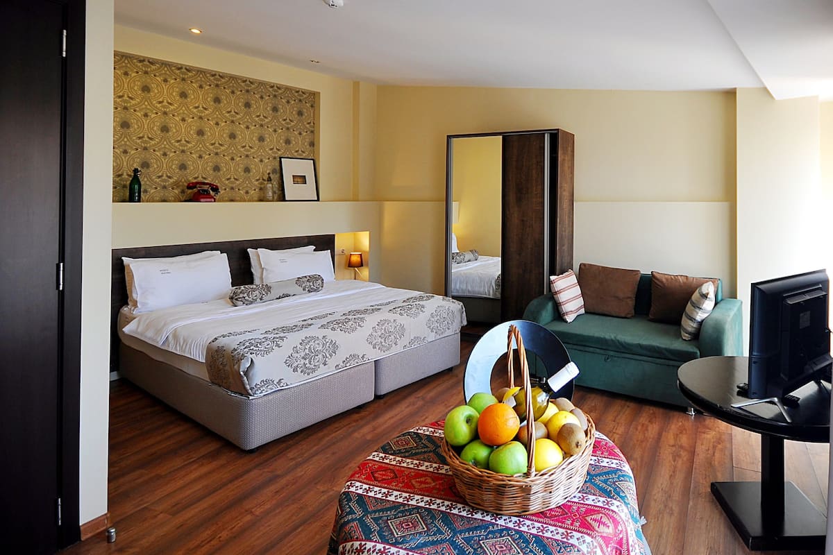 A hotel room with a bed, a sofa, a TV, and a fruit basket.