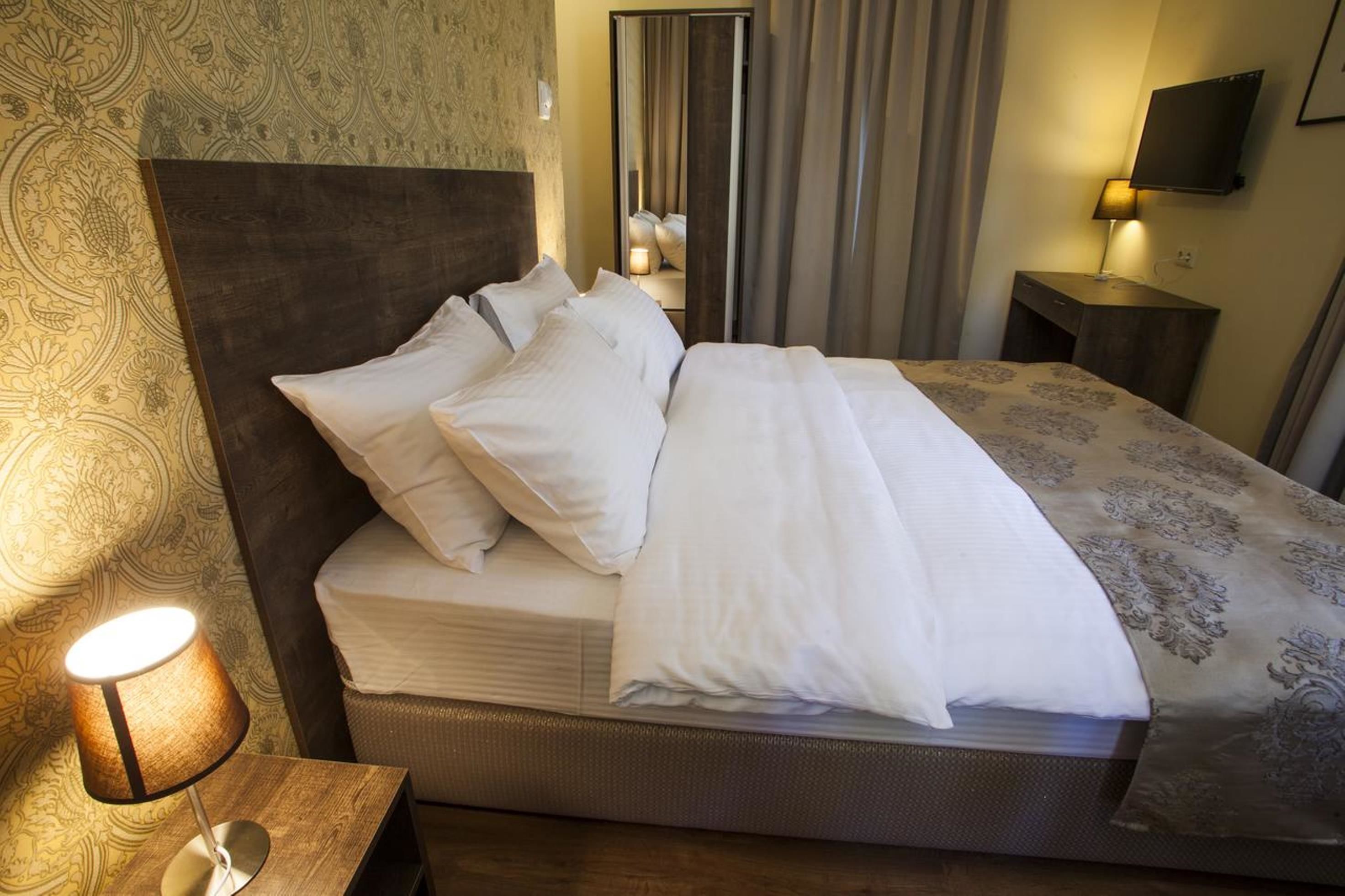A neatly made bed with white linens, a wooden headboard, and a bedside lamp.