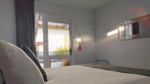 Habitación de hotel con cama, una silla, una ventana con cortinas, una lámpara fijada a la pared y un cartel de seguridad contra incendios.