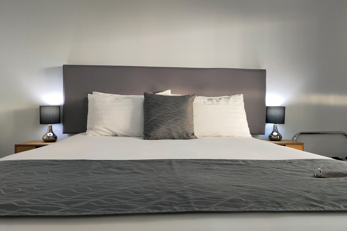 A neatly made bed with a grey textured blanket, two bedside lamps, and a dark headboard.