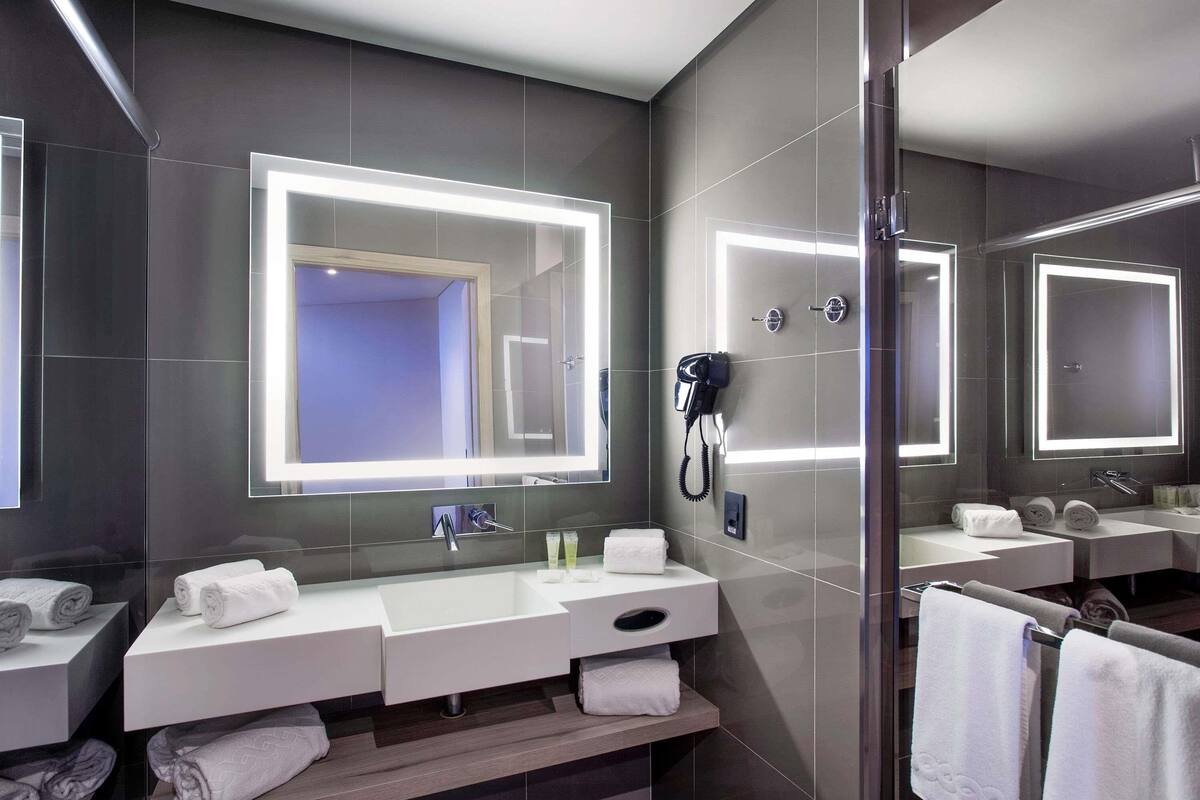 A modern bathroom with a large mirror, a hairdryer, and neatly folded towels.