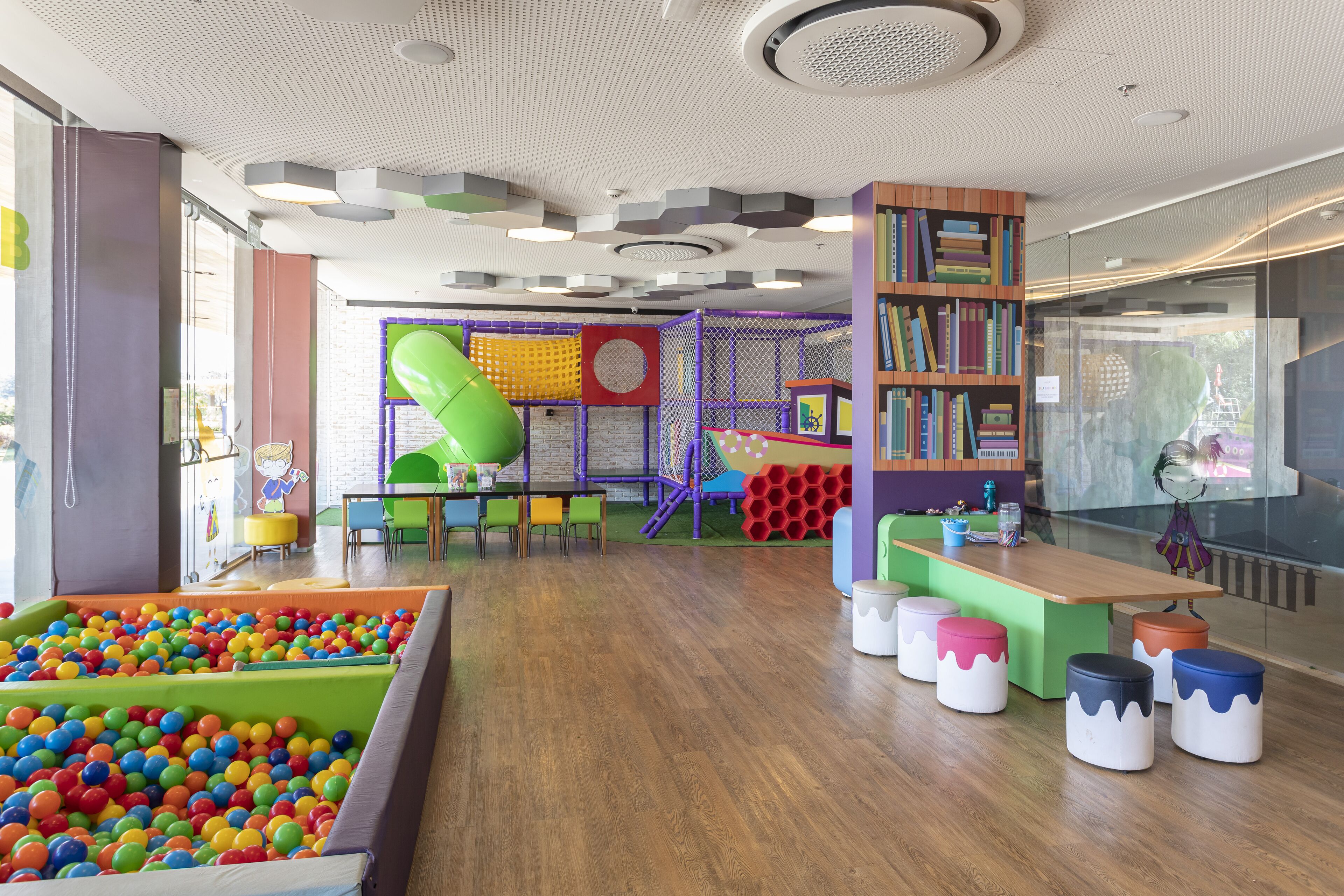 Zona de jocs infantil amb bressol de pilotes, estructures de joc de colors i una estanteria de fusta.