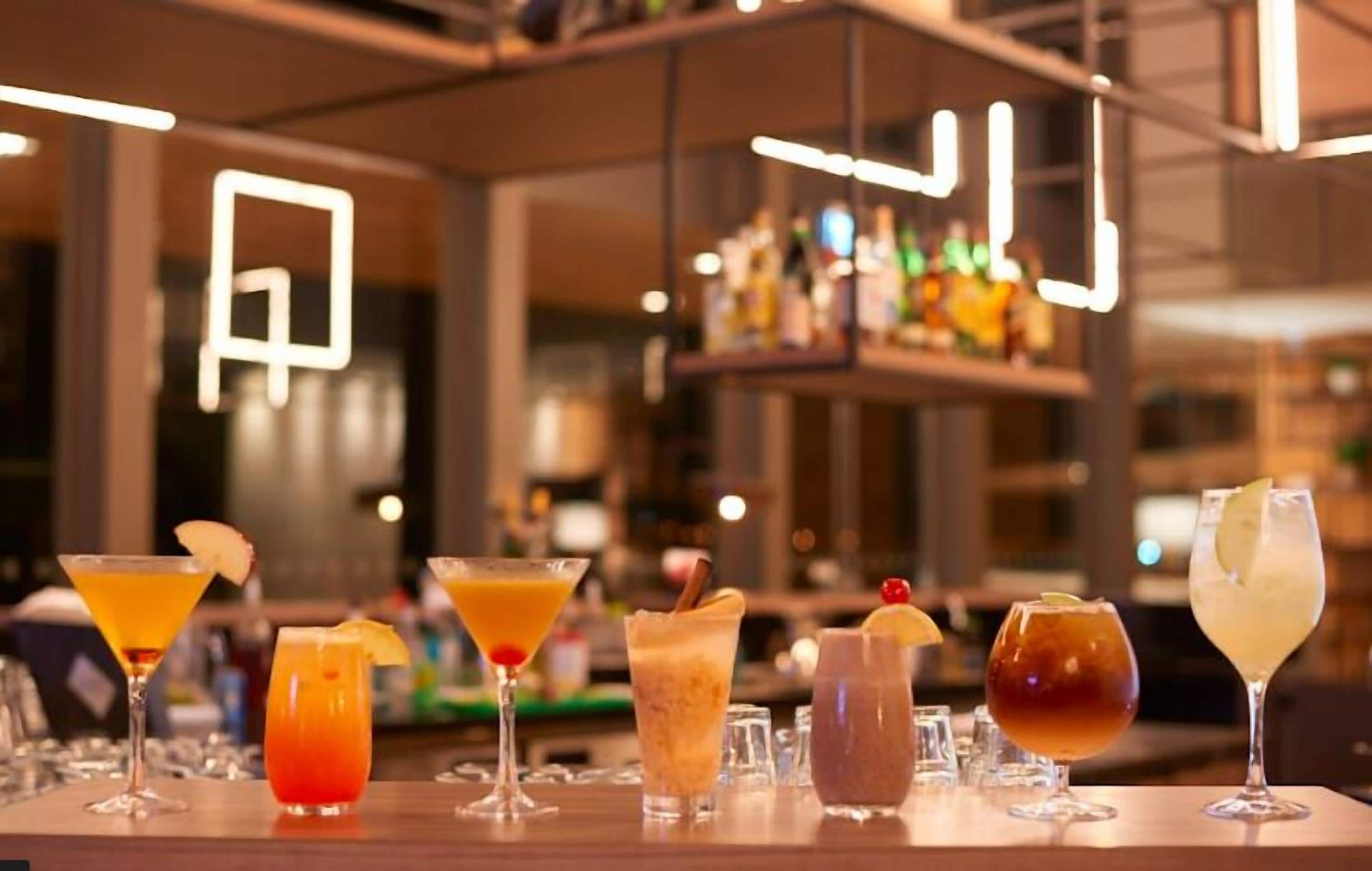 Zona de bar con varios cócteles y una estantería bien surtida al fondo.