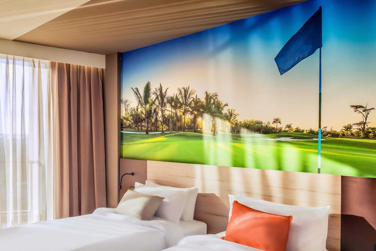 A hotel room with two beds, a large window with curtains, and a wall mural of a golf course.