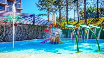A swimming pool with a water play area, surrounded by a fence and trees.