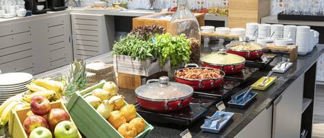 Un bufé con diversos alimentos, entre ellos frutas, ensaladas y platos calientes.