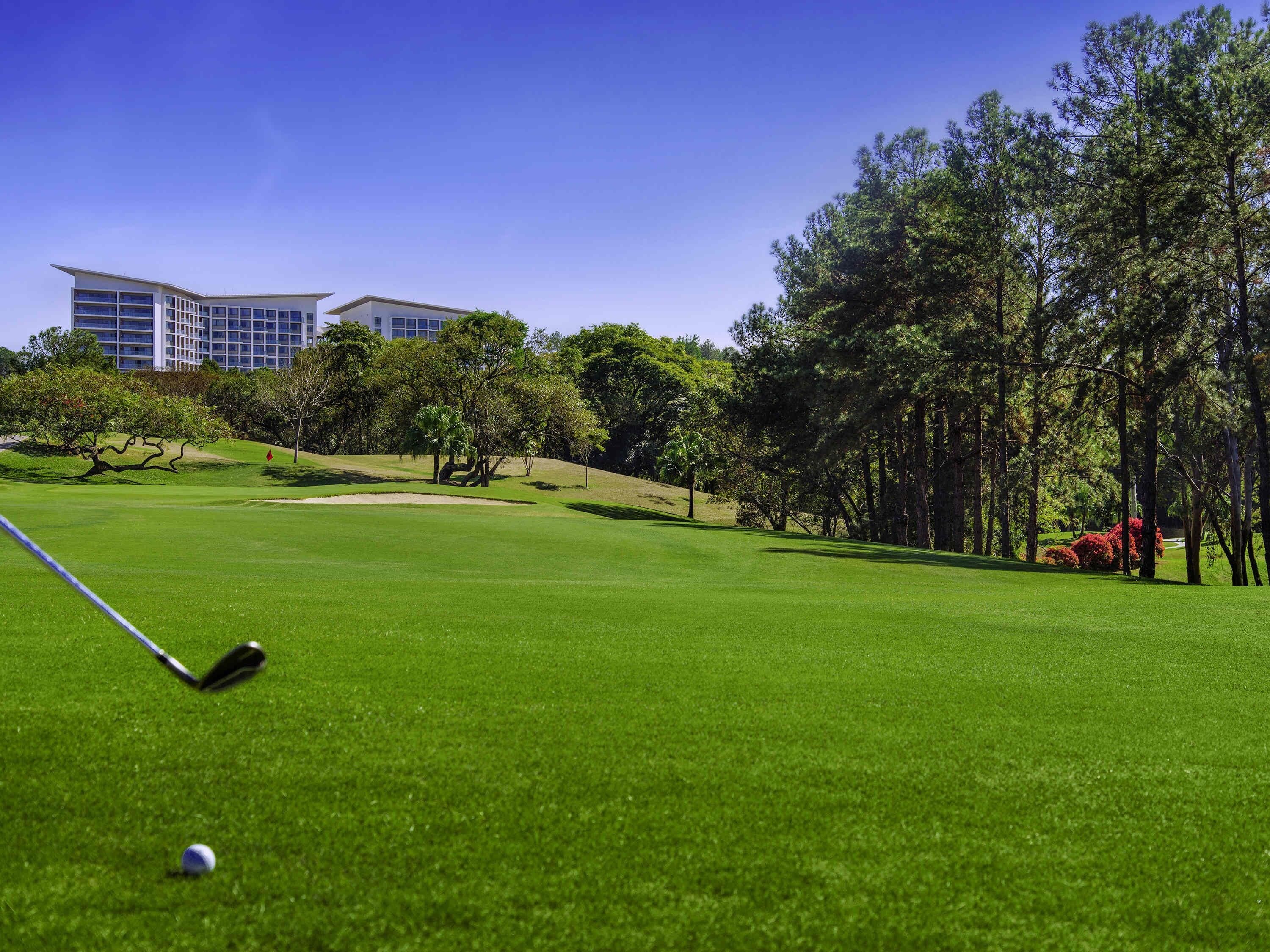 Un terrain de golf avec un ciel dégagé, un green d’entraînement et un bâtiment en arrière-plan.