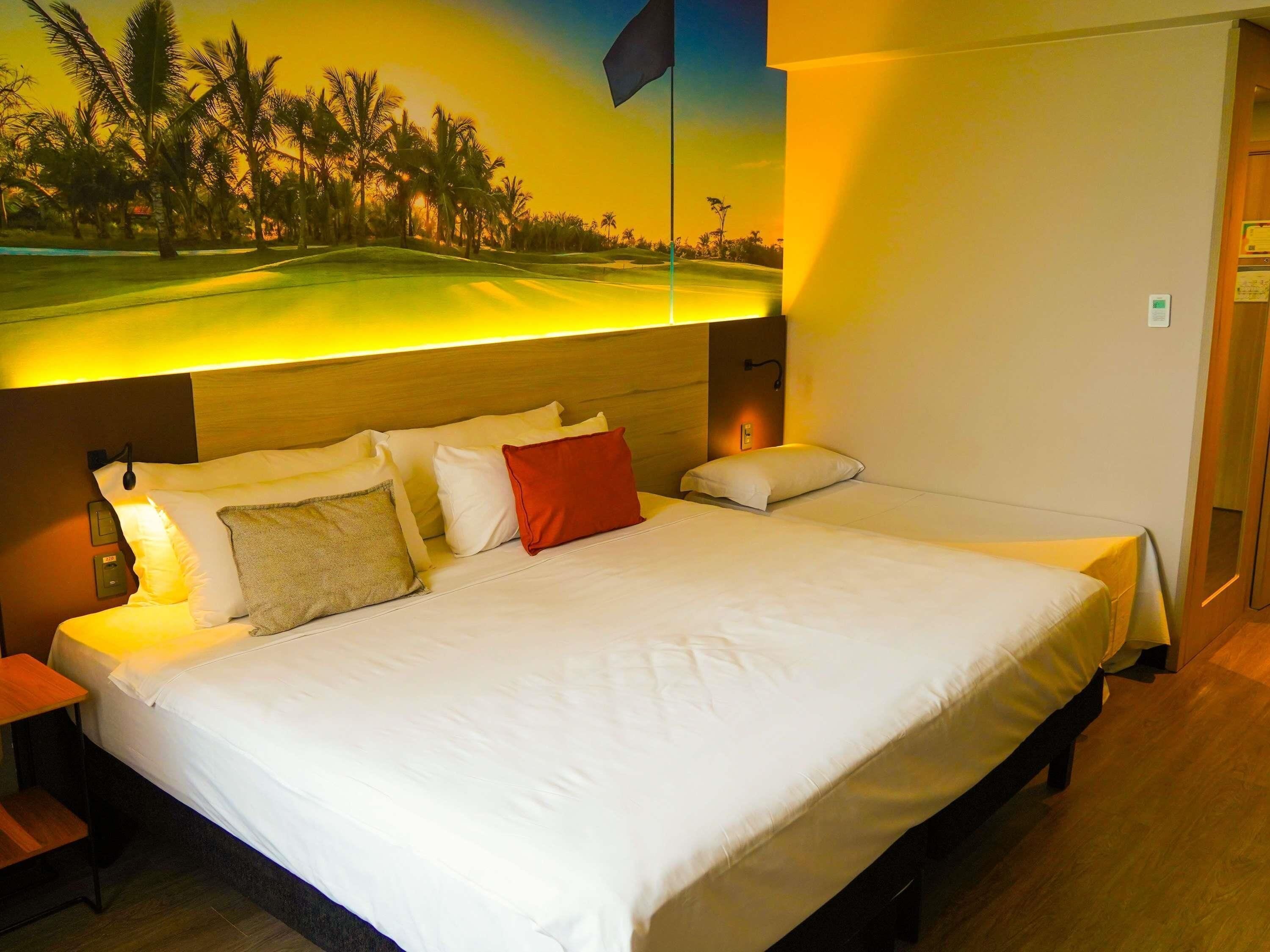 Habitación de hotel con una cama grande, una mesita de noche, una lámpara de pared y un mural de un campo de golf.