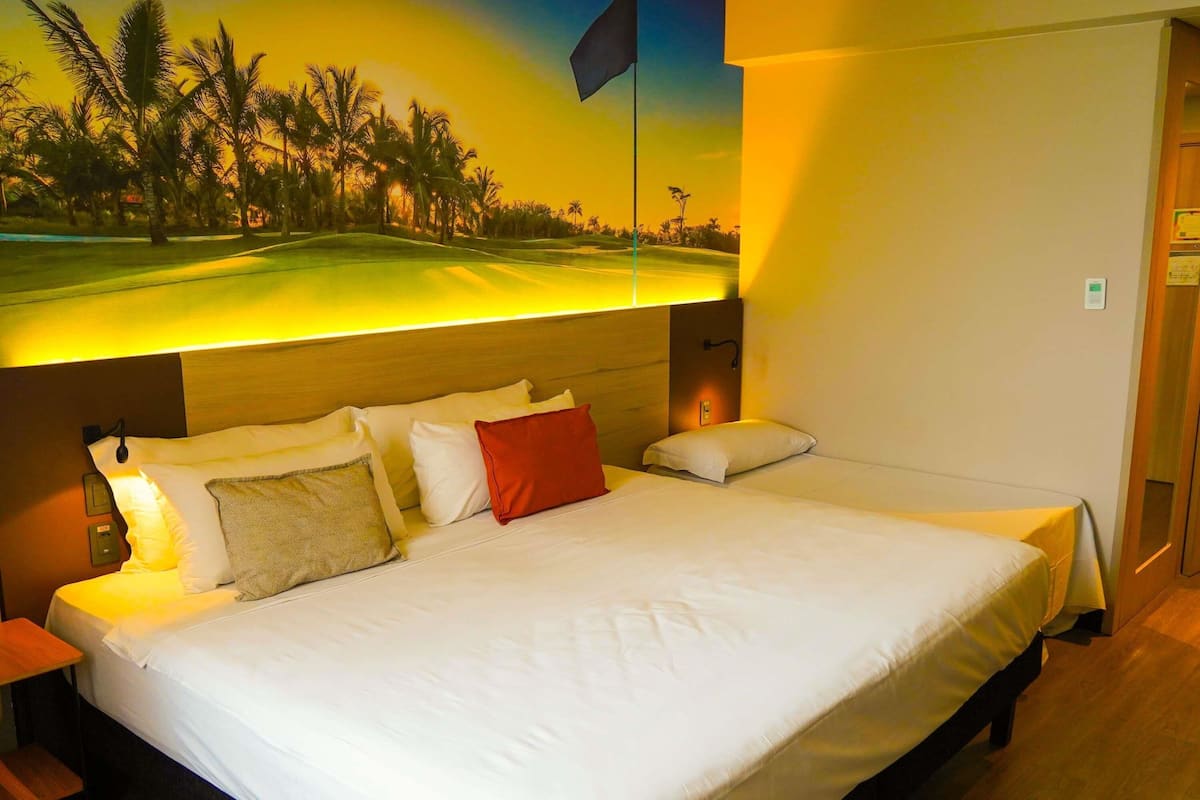 A hotel room with a large bed, a nightstand, a wall-mounted lamp, and a mural of a golf course.